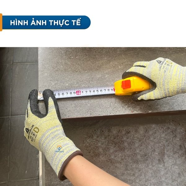 Hình ảnh thực tế găng tay Delta Plus Venicut52 đang cầm thước dây vàng đo cạnh bậc đá, ngón tay giữ đầu thước