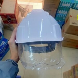 Người công nhân đang cầm mũ bảo hộ COV E002 màu trắng với kính trong suốt hạ xuống, trong môi trường kho hàng.